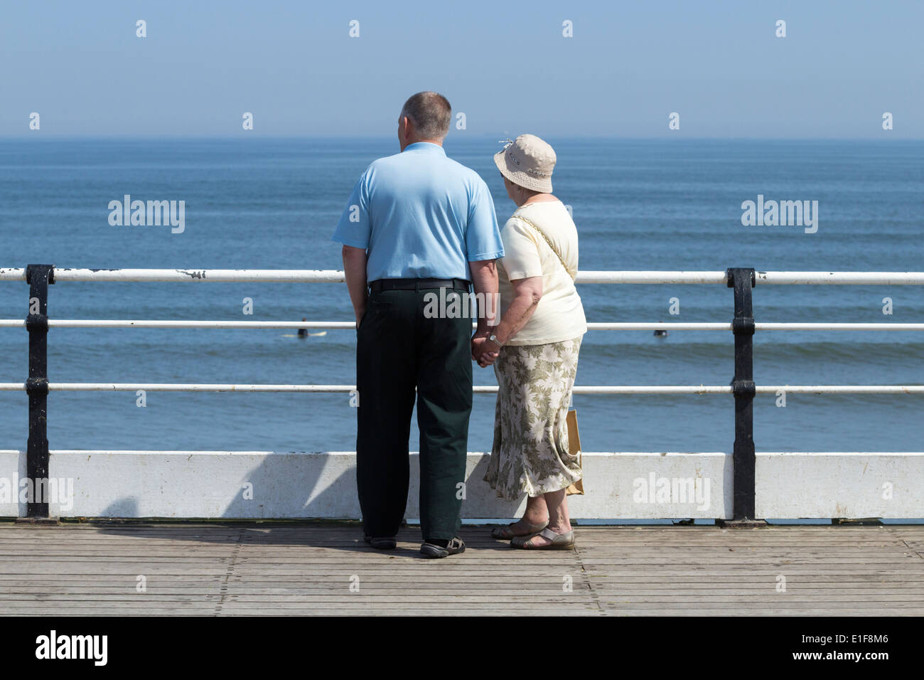Elderly couple holding hands watching surfers from Saltburn`s Victorian pier Stock Photo